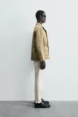 Pantalón chino de corte ajustado, color beige, con bolsillos laterales y bolsillos traseros de vivo. Cuenta con cierre frontal de cremallera y botón.