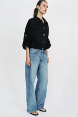 Blusa negra de cuello solapa y manga corta, con bolsillos con solapa en el pecho, bajo elástico y cierre frontal con botones.