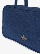 Bolso de hombro tipo cartera confeccionado en denim azul, con diseño rectangular, cierre superior y asas largas. Presenta el logo del Trifolio metálico en la parte frontal.