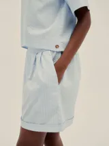 Shorts celestes a rayas verticales, de tiro alto y corte holgado, con pinzas en el frente y detalle de Polonio en cobre.