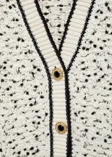 Cardigan de punto grueso con diseño jaspeado en blanco y negro. Presenta cuello en pico, cierre frontal con botones efecto joya, dos bolsillos de parche delanteros y detalles en contraste negro en los bordes.