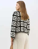 Cardigan abierto de tejido de punto calado con diseño geométrico y floral bicolor. Presenta escote en V, mangas largas y cierre frontal con tiras para anudar. Incluye detalles de vivos a contraste en el contorno del escote, puños y ruedo.