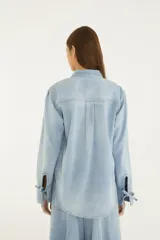 Camisa de jean de corte amplio con cuello camisero, cierre frontal con botones metálicos y grandes bolsillos frontales con solapa.