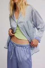 Conjunto de pijama de dos piezas, compuesto por una camisa de manga larga con estampado geométrico, cuello y botonadura frontal, y un pantalón largo fluido de color celeste con cintura elastizada, cordón de ajuste y detalles estampados en los dobladillos.