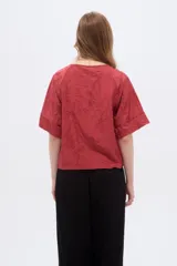 Blusa de viscosa color marrón rojizo, con diseño holgado, cuello a la base, mangas cortas y detalle de bordado floral en tono sobre tono.