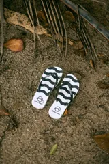 Chancletas de playa con diseño de ondas negras sobre fondo blanco, tiras de dedo negras y logo de la marca en la suela.