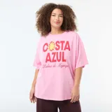 Camiseta oversize de manga corta color rosado, con cuello redondo y estampa frontal con la leyenda "Costa Azul" en rojo y amarillo.