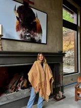 Ruana artesanal color crudo con rayas horizontales color ladrillo y flecos.