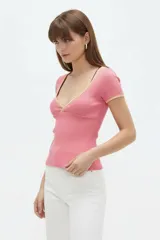 Remera rosada de manga corta, confeccionada en algodón con textura acanalada, corte ajustado al cuerpo y escote en V profundo con ribetes contrastantes en tono amarillo claro.