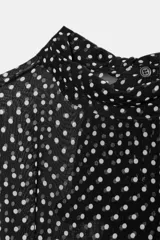Blusa negra con estampado de lunares blancos, cuello redondo con lazadas y manga larga con puños ajustados. El bajo es ajustable con cordones.