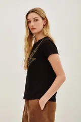 Remera negra de manga corta con cuello redondo y un aplique grande en forma de rayo. El rayo está decorado con lentejuelas doradas y negras.