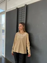 Remera color beige de manga larga con cuello redondo y bordado floral blanco en el escote.