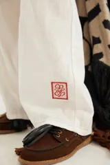 Pantalón de corte recto y tiro medio con costuras a la vista, bolsillos delanteros y traseros, y un detalle de pin de la marca en el ruedo.
