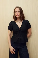 Top negro de textura tramada, con escote en V y frunce central. Posee mangas cortas con elástico y un ruedo con volado sutil.