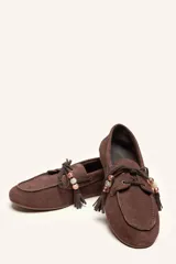 Mocasín estilo náutico de gamuza marrón, con cordones de cuero, borla decorativa y cuentas de colores en el empeine.