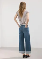 Jeans estilo wide leg de tiro medio con diseño de cinco bolsillos, trabillas para cinturón, cierre de botón y cremallera, y bajo vuelto.