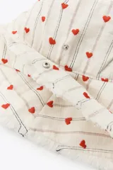 Gorro tipo bucket de algodón, color crudo, con rayas verticales finas en tono neutro y pequeños corazones rojos bordados distribuidos por toda la superficie. Presenta ala ancha con terminación deshilachada.