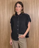 Camisa de denim negro con mangas cortas, cuello camisero, cierre frontal con botones y costuras a contratono.
