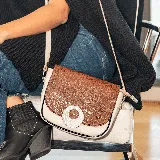 Bandolera de cuero vacuno color tostado y beige, con correa larga ajustable y removible. Tiene bolsillo con cierre en la tapa trasera y cierre superior. El interior está forrado y tiene un bolsillo para el celular.
