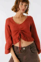 Top cropped color terracota con escote en V, mangas largas estilo balloon y detalle de jareta ajustable con lazo en el centro del busto. El ruedo inferior tiene un pequeño volado.