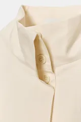 Camisa de popelín color beige, con cuello subido y manga larga acabada en puño. Cierre frontal con botones ocultos por solapa.