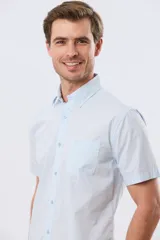 Camisa de manga corta color celeste con diseño de microcuadros, cuello camisero, cierre frontal con botones y un bolsillo aplicado en el pecho.