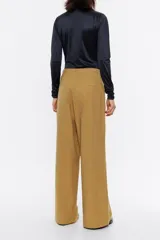 Pantalón de vestir color marrón claro, de corte ancho, con pinzas en la parte delantera, bolsillos laterales y trabillas en la cintura.