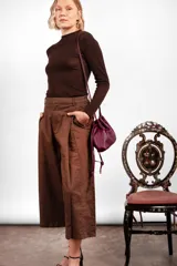 Bolso tipo sobre color bordó con diseño fruncido inspirado en la forma de un dumpling, con cierre ajustable mediante cordones y correa larga desmontable.