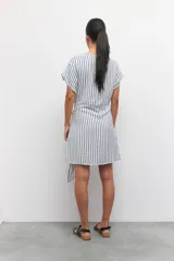 Vestido corto a rayas verticales azules y blancas, de corte suelto y manga corta. Presenta un lazo en uno de sus laterales.
