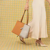 Cartera tipo tote de cuero sintético con diseño combinado en tono gris y blanco, textura granulada, asas largas para el hombro y cierre superior.
