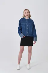 Campera corta de denim azul oscuro, con cuello mao deshilachado y botones plateados frontales. Las mangas largas tienen puños anchos con estampado de rayas verticales en tonos celestes y blancos.