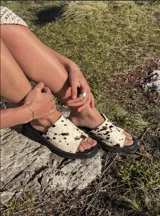 Sandalias tipo ojotas con base negra y tira ancha de pelo sintético con estampado animal print de vaca.