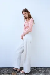 Chaqueta de punto pointelle en color rosado, con cuello redondo, manga larga y bolsillos delanteros de parche. Cuenta con cierre frontal de botones claros.