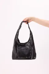 Bolso hobo negro de símil cuero con tachas plateadas en el bolsillo frontal y en el asa.