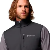 Campera cortaviento Columbia modelo Ascender, confeccionada en tejido softshell con tecnología Omni-Shield repelente al agua. Presenta diseño bicolor en tonos gris y grafito, cuello alto con protector de mentón, cierre frontal completo, bolsillos laterales y en el pecho con cremallera, y puños ajustables.
