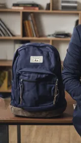 Mochila de tela Oxford azul con base de nobuk, cuenta con un compartimento principal amplio y un bolsillo frontal con cierre. Incluye correas de hombro acolchadas y tiradores de cierre en cuero.