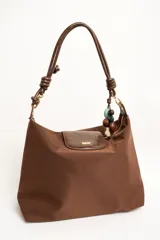 Cartera tipo shopper color marrón, con solapa frontal decorativa en tono más oscuro y tiras con nudos. Incluye herrajes dorados y un charm colgante con cuentas de madera.