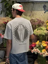Remera gris de manga corta con corte regular, de la marca Kaboa Industries, con estampa en la espalda que presenta un esqueleto dentro de un ataúd rodeado por alas oscuras y las leyendas WAKE UP y Kaboa Industries.