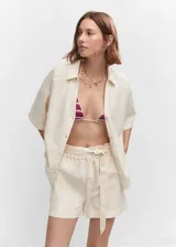 Short de tiro alto confeccionado en una mezcla de algodón y lino. Presenta un diseño recto y corto, con cintura elástica y un lazo desmontable para ajustar. Incluye dos bolsillos laterales.