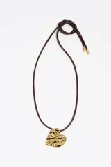 Collar con cordón largo de cuero marrón y dije colgante dorado en forma de corazón con diseño texturizado irregular y acabado metálico brillante. Cuenta con terminales metálicas doradas en los extremos del cordón.