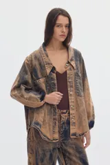 Camisa de denim oversize, con efecto acid wash en tonos marrones y negros, mangas abullonadas, cuello en V con solapa y bolsillos frontales con solapa.
