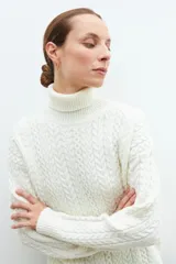 Polera color crudo con cuello alto y tejido con diseño de trenzas.