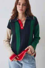 Buzo estilo polo de tejido de punto con diseño a rayas verticales en bloques de color azul marino, verde, beige y rojo. Presenta cuello polo con cartera frontal de botones, mangas largas con puños en contraste y tajos laterales en el ruedo.