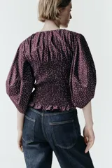 Blusa de color bordó con estampado de lunares claros, confeccionada con cuerpo en nido de abeja elástico, cuello redondo y mangas abullonadas por debajo del codo.
