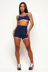 Top deportivo de poliamida color azul marino, de modelado slim y ajuste ceñido al cuerpo. Presenta escote redondo y tiras en color blanco contrastante que recorren los bordes superior e inferior, con el logo de la marca estampado en el centro del pecho.