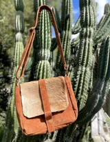 Morral de cuero gamuzado color tostado, con correa regulable, solapa frontal de pelo vacuno y cierre central con tira vertical.