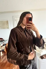 Campera de gamuza color chocolate con diseño de flecos en el pecho, espalda y mangas. Presenta cuello clásico, cierre frontal con botones y bolsillos laterales.
