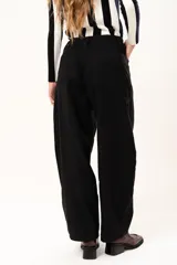 Pantalón de tiro medio con silueta curvada, más ancha en la zona de los muslos y rodillas, con cierre frontal de cremallera y botón.