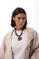 Collar corto con dije central en forma de flor doble, texturada y pintada a mano en tonos marrones. La cadena está compuesta por piedras naturales irregulares en tonos verdes y tierra, con cierre de acero quirúrgico ajustable.