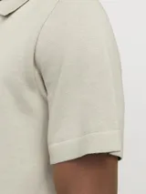 Polo de punto color beige con cuello polo, cierre frontal parcial con cremallera y mangas cortas. Presenta un tejido estructurado y corte regular.